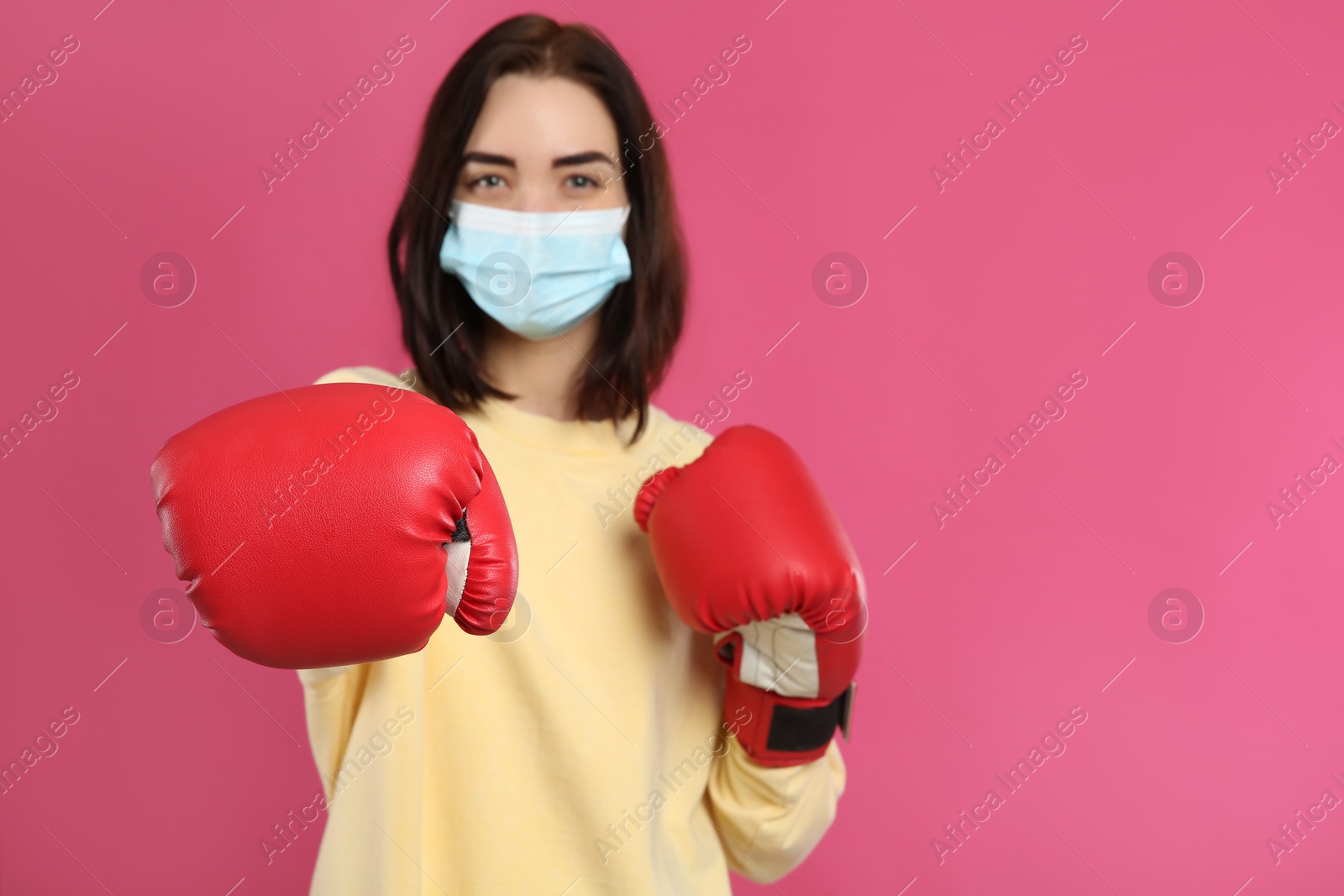 Photo of Woman with protective mask and boxing gloves on pink background, space for text. Strong immunity concept