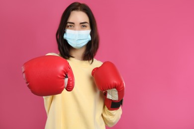 Photo of Woman with protective mask and boxing gloves on pink background, space for text. Strong immunity concept