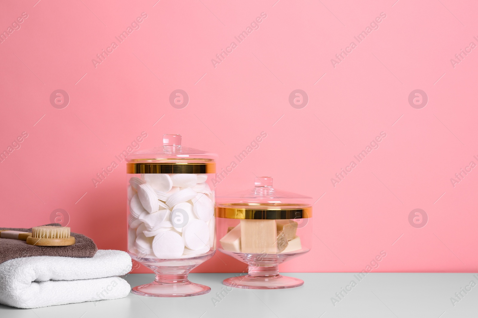 Photo of Composition of glass jar with cotton pads on table near pink wall. Space for text