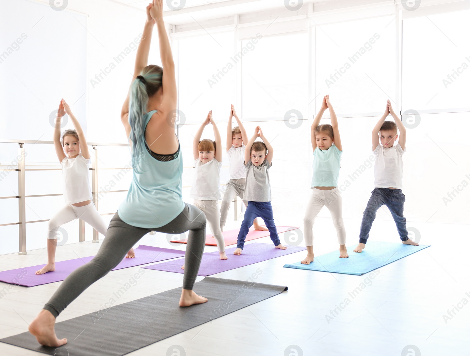 Photo of Little children and their teacher practicing yoga in gym