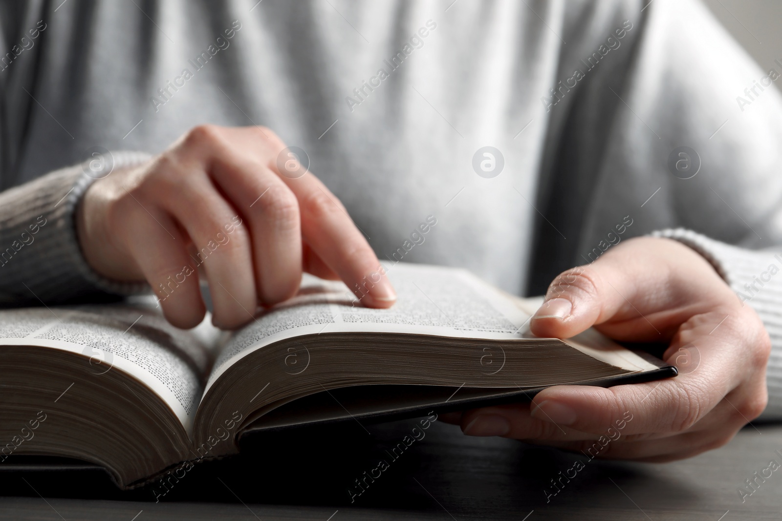 Photo of Woman reading Bible at wooden table, closeup