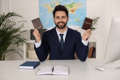 Photo of Happy manager holding passports at desk in travel agency