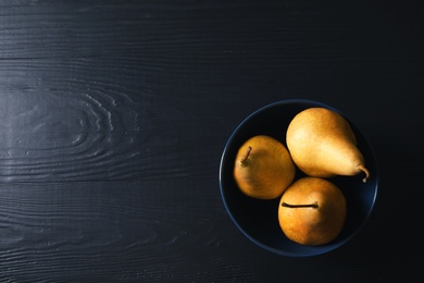 Bowl with ripe pears on black wooden background, top view. Space for text