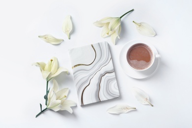 Beautiful lily flowers, cup of coffee and notebook on white background, flat lay 