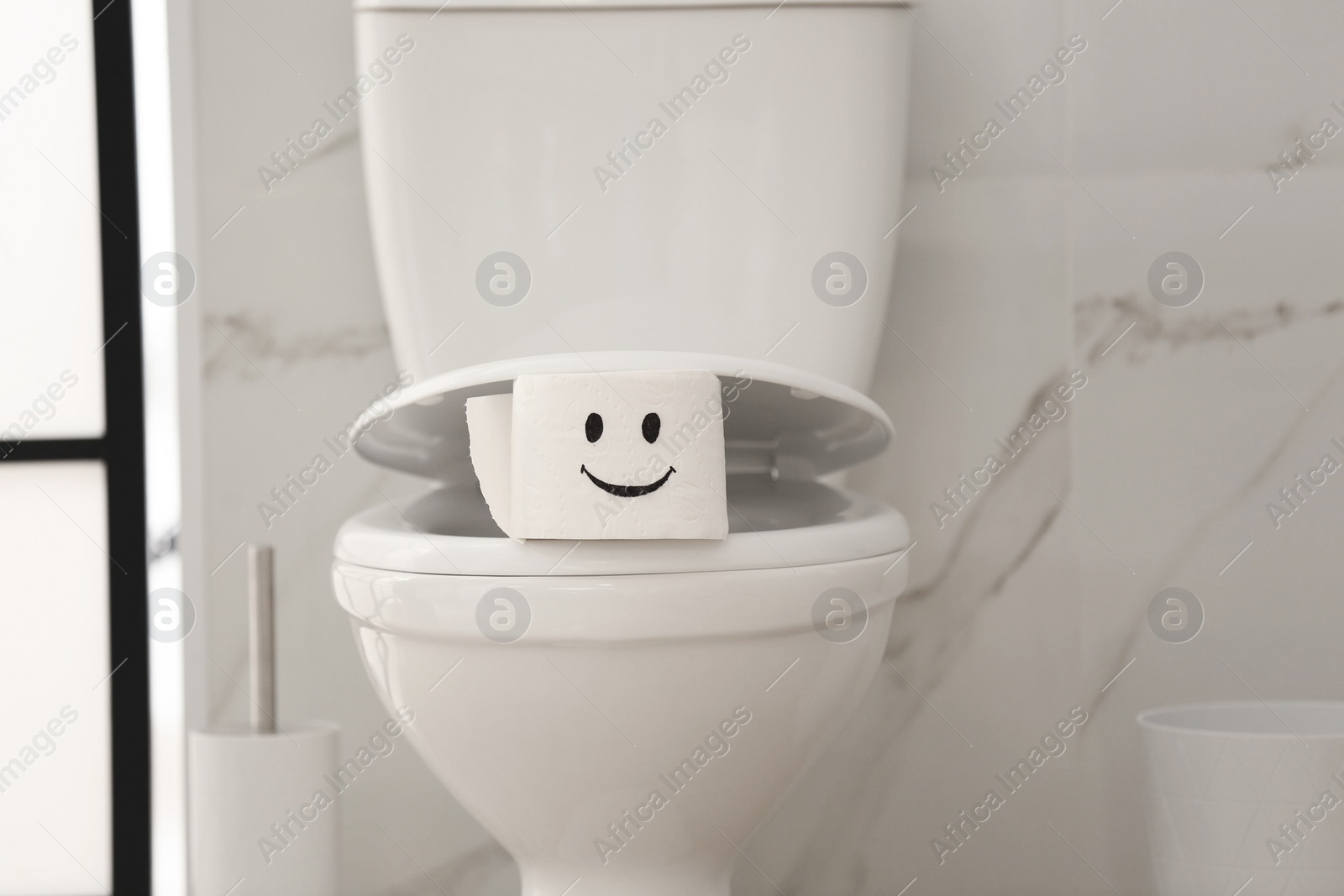 Photo of Roll of paper with funny face on toilet bowl in bathroom