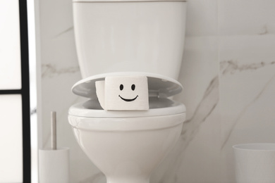 Photo of Roll of paper with funny face on toilet bowl in bathroom
