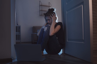 Photo of Upset teenage girl with laptop on floor in dark room. Danger of internet