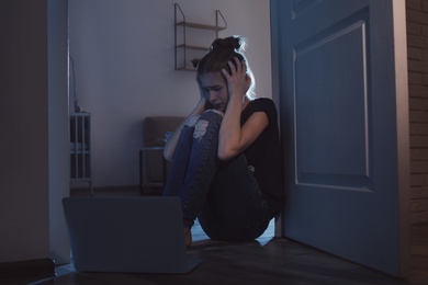 Upset teenage girl with laptop on floor in dark room. Danger of internet