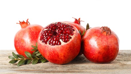 Photo of Fresh pomegranates and green leaves on wooden table against white background