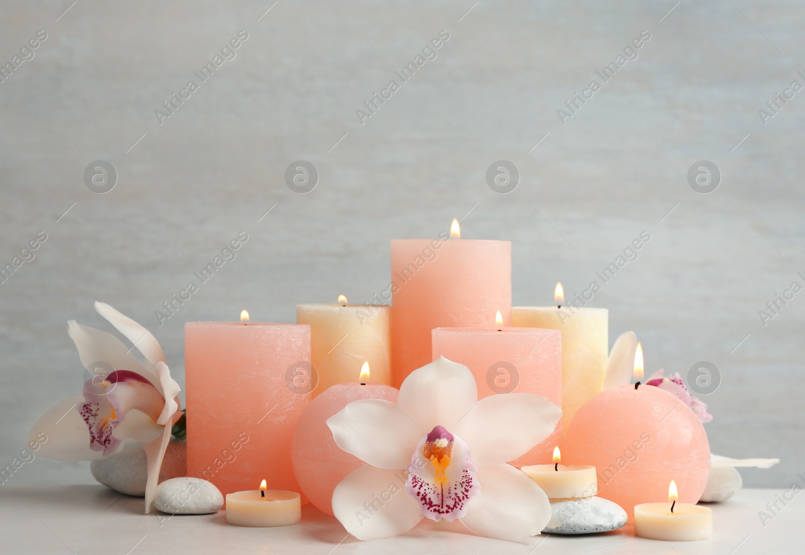 Photo of Beautiful composition with candles and flowers on table against light background