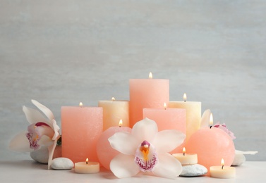 Photo of Beautiful composition with candles and flowers on table against light background