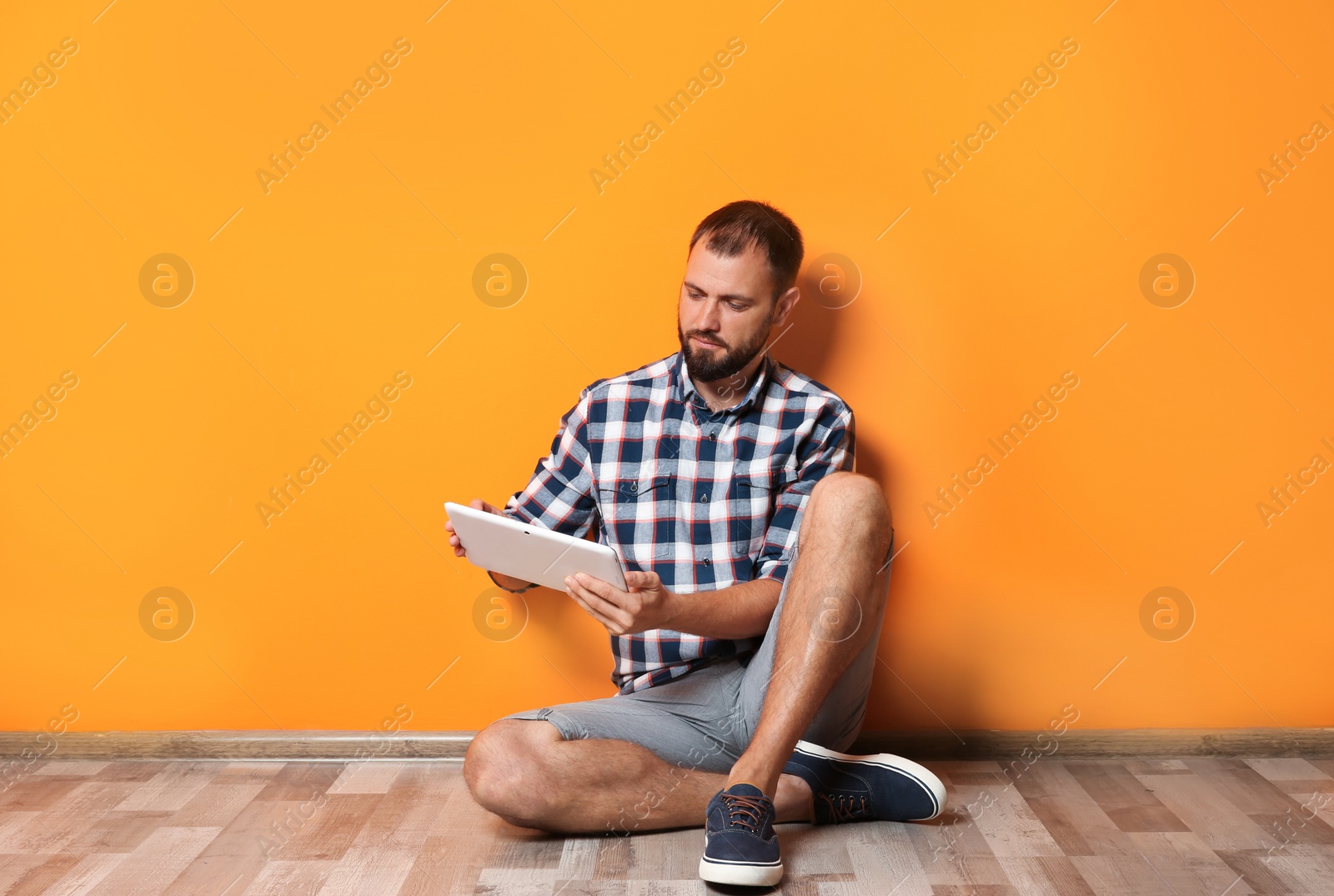 Photo of Man in casual clothes with tablet near color wall