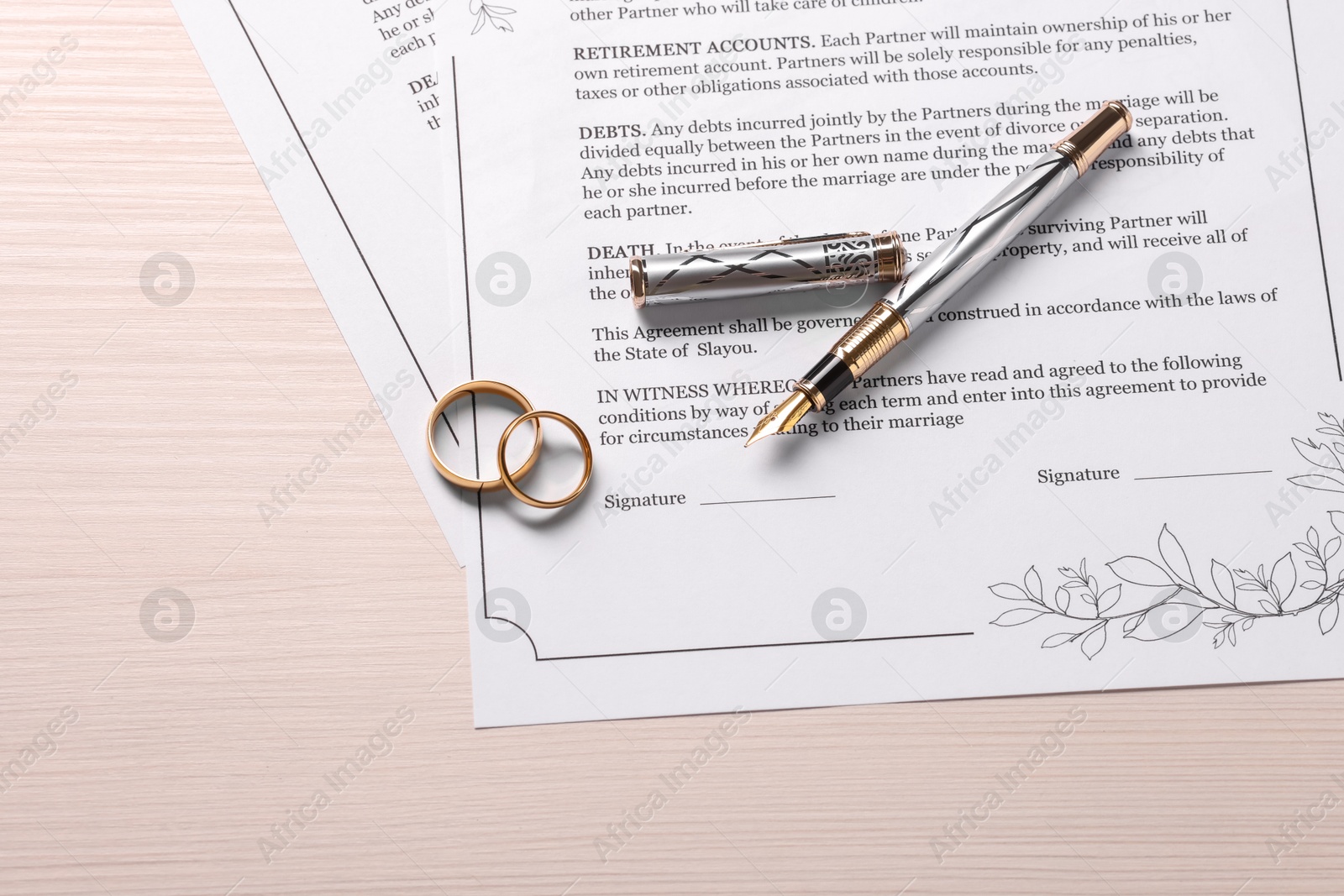 Photo of Marriage contracts, gold rings and pen on light wooden table, top view