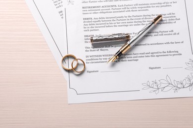 Photo of Marriage contracts, gold rings and pen on light wooden table, top view