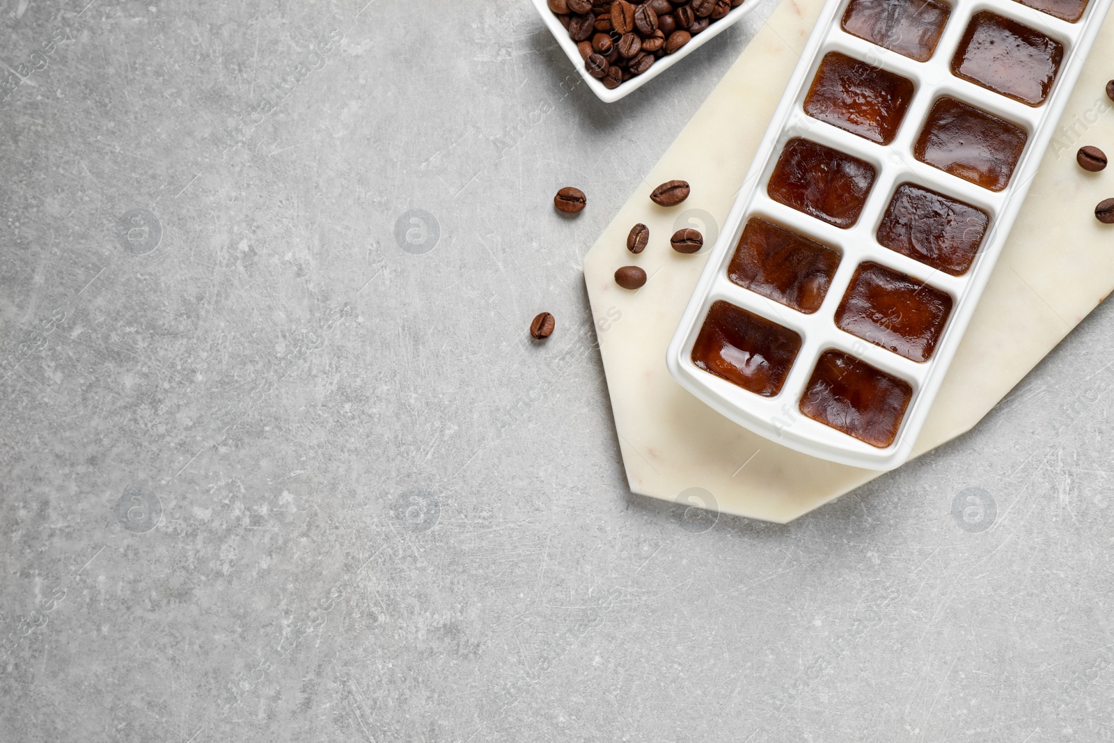 Photo of Ice cubes with coffee beans in tray on grey table, flat lay. Space for text