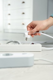 Woman inserting power plug into extension cord on floor indoors, closeup. Electrician's professional equipment