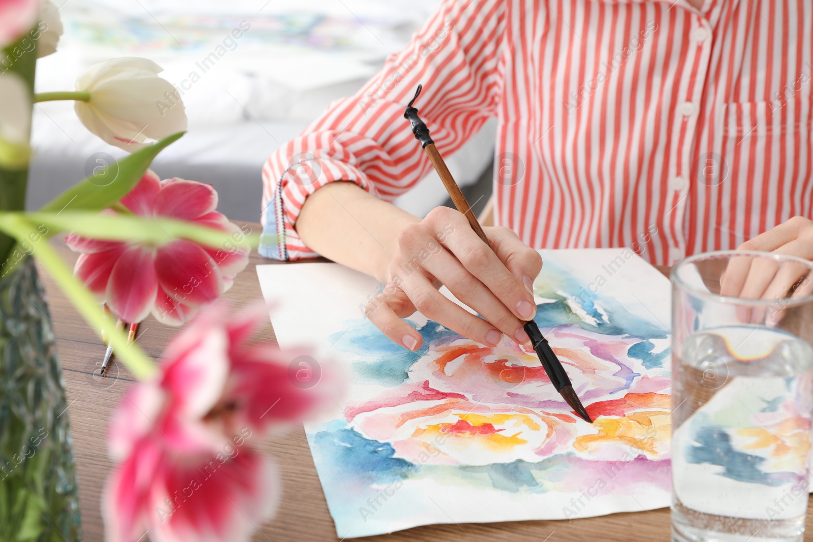 Photo of Woman painting flowers with watercolor at wooden table indoors, closeup. Creative artwork