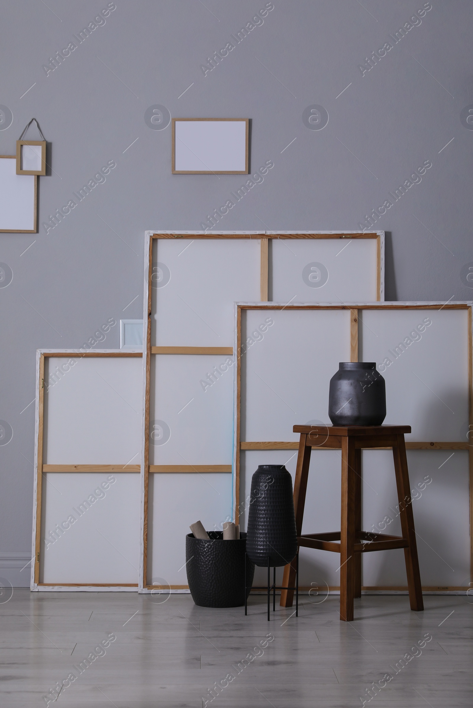 Photo of Many paintings, wooden stool and vases near grey wall in artist's studio