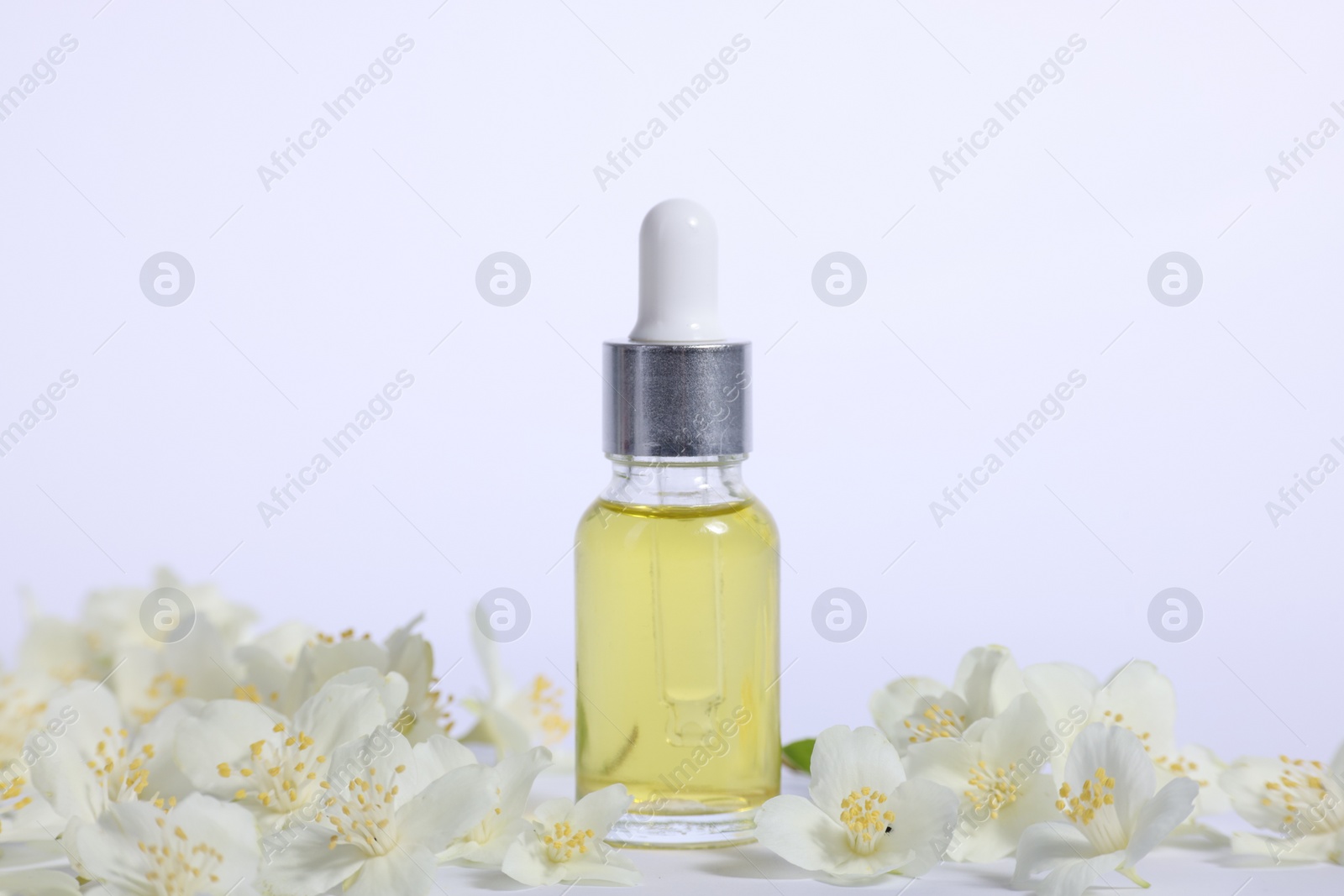 Photo of Essential oil in bottle and beautiful jasmine flowers on white background