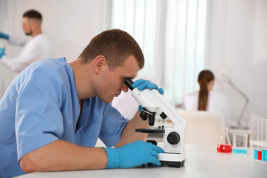 Photo of Scientist using microscope at table and colleagues in laboratory. Medical research