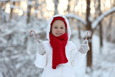 Photo of Cute little girl with candy canes in winter park