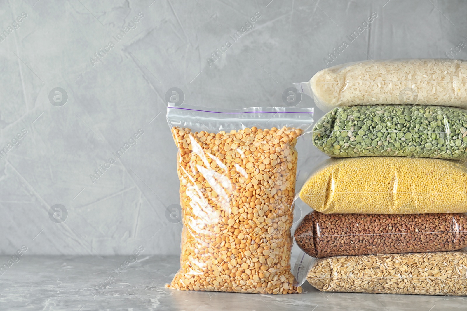 Photo of Different types of legumes and cereals on grey marble table, space for text. Organic grains