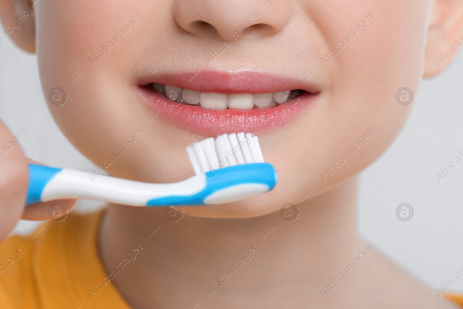 Photo of Girl brushing her teeth with toothbrush on light grey background, closeup