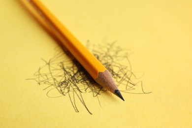 Photo of One sharp graphite pencil and scribbles on yellow background, closeup