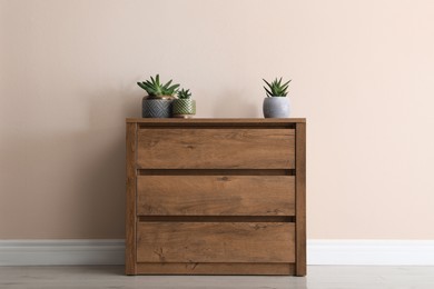 Photo of Wooden chest of drawers with houseplants near beige wall