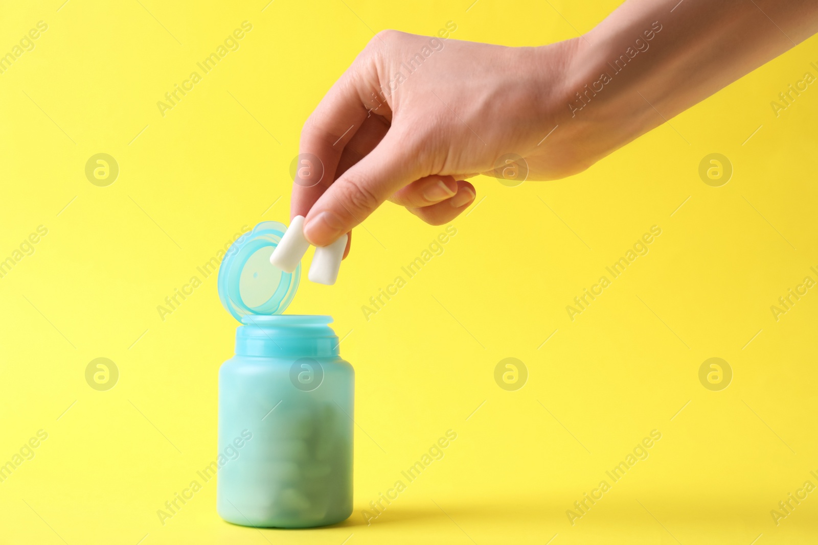 Photo of Woman taking chewing gums from jar on yellow background, closeup