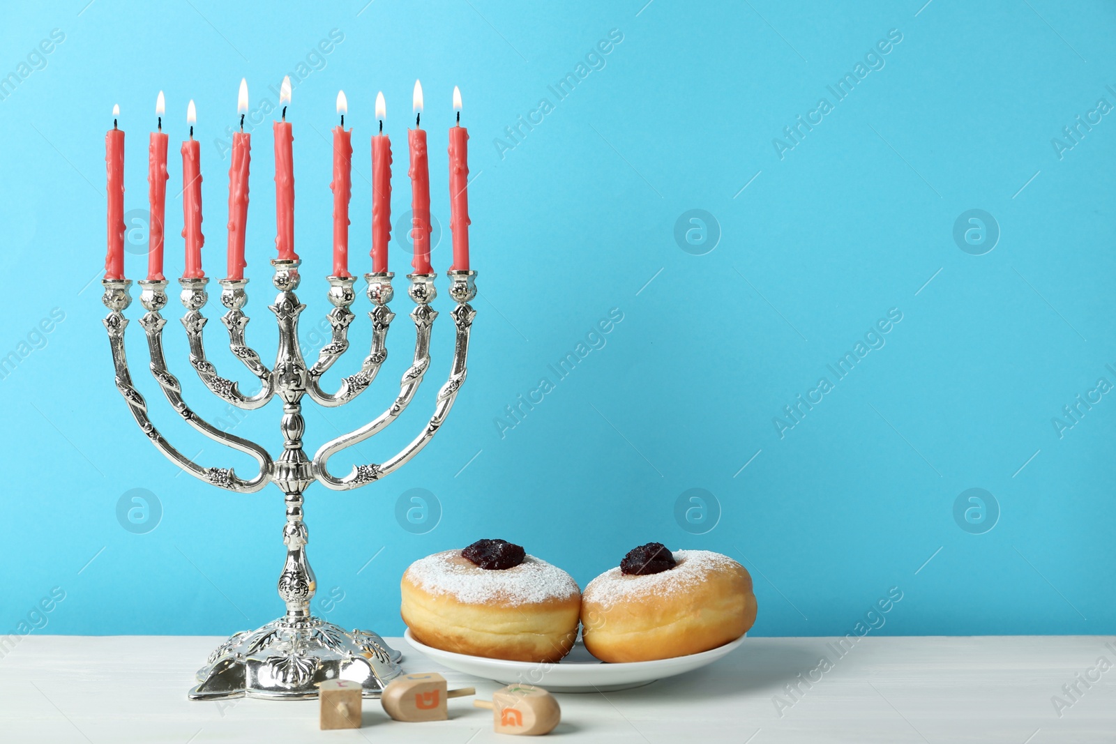 Photo of Silver menorah, dreidels with He, Pe, Nun, Gimel letters and sufganiyot on white table, space for text. Hanukkah symbols