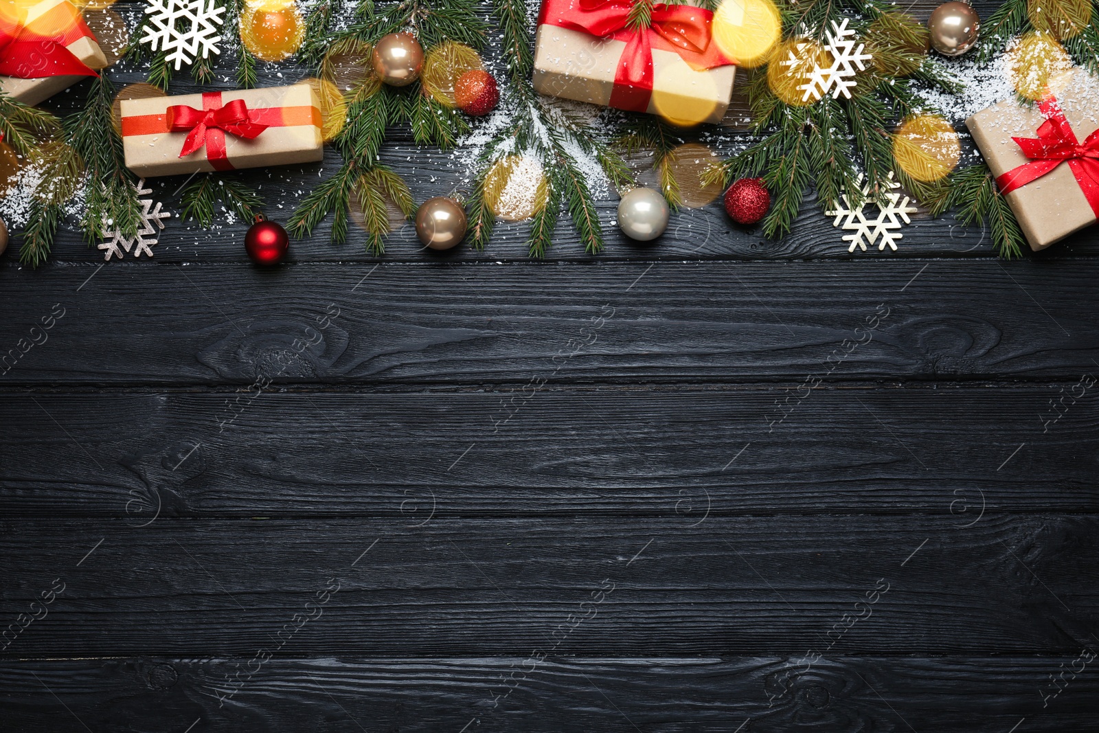 Photo of Christmas greeting card with space for text. Flat lay composition of fir tree branches and festive decor on black wooden background