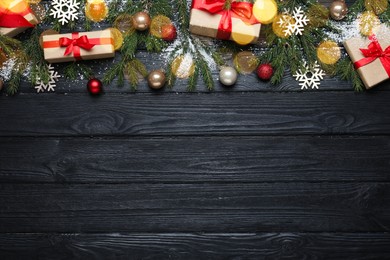 Photo of Christmas greeting card with space for text. Flat lay composition of fir tree branches and festive decor on black wooden background