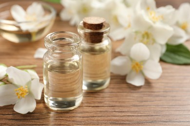 Photo of Jasmine essential oil and fresh flowers on wooden table, space for text