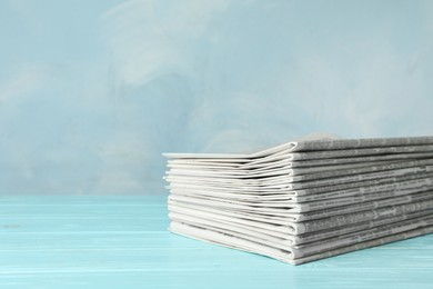 Photo of Stack of newspapers on light blue wooden table, space for text. Journalist's work