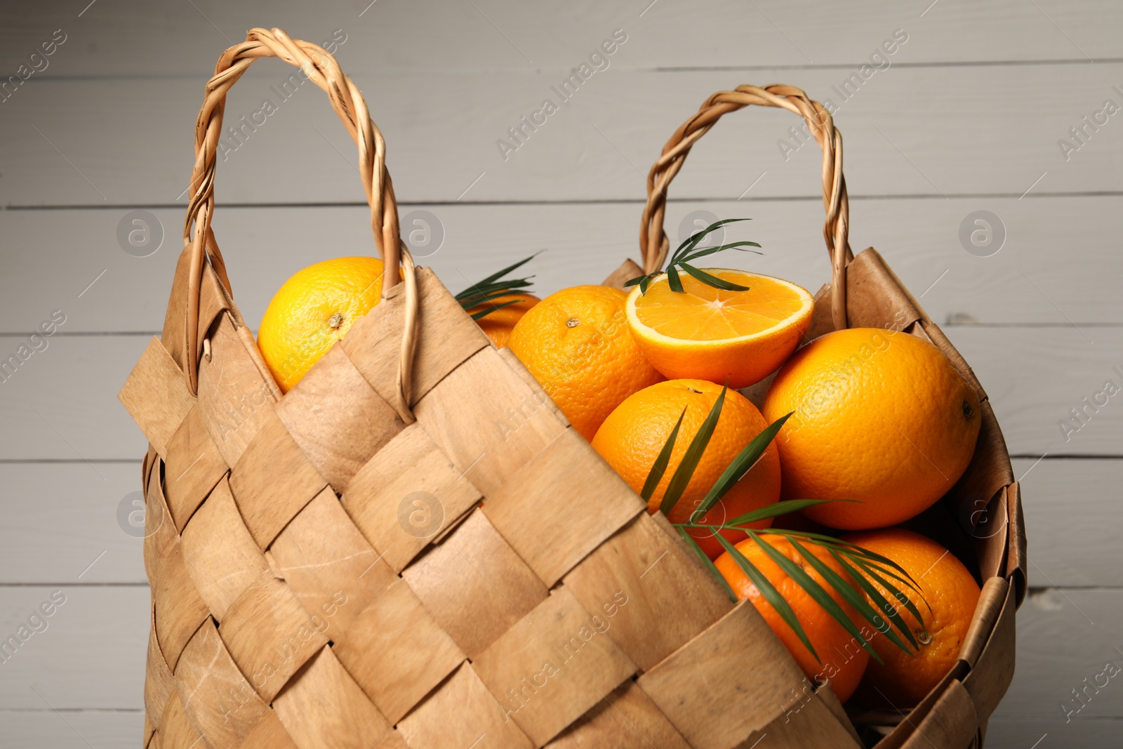 Photo of Wicker basket with whole and cut ripe oranges on wooden background, closeup