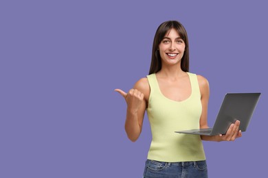 Photo of Special promotion. Happy woman with laptop pointing at something on violet background, space for text