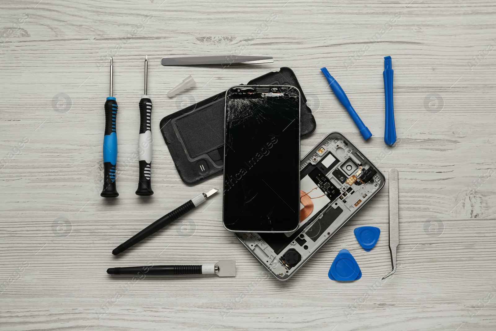 Photo of Damaged smartphone and repair tools on wooden background, flat lay