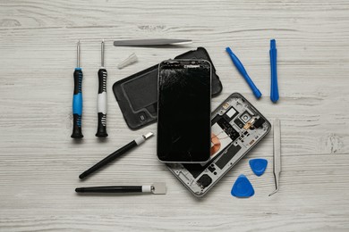 Damaged smartphone and repair tools on wooden background, flat lay