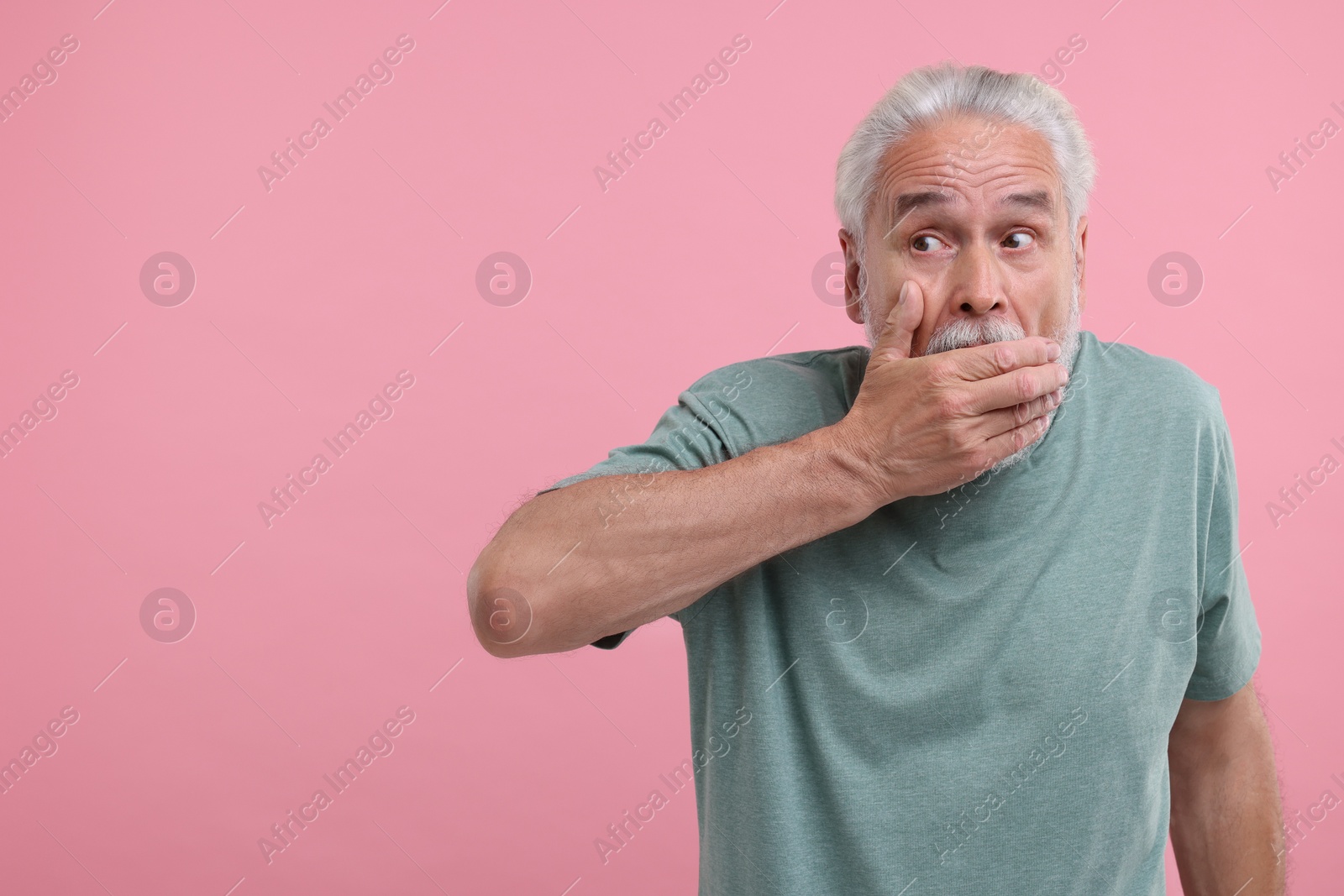 Photo of Embarrassed senior man covering mouth on pink background. Space for text