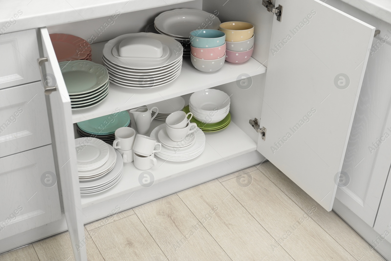 Photo of Clean plates and other crockery on shelves in cabinet indoors