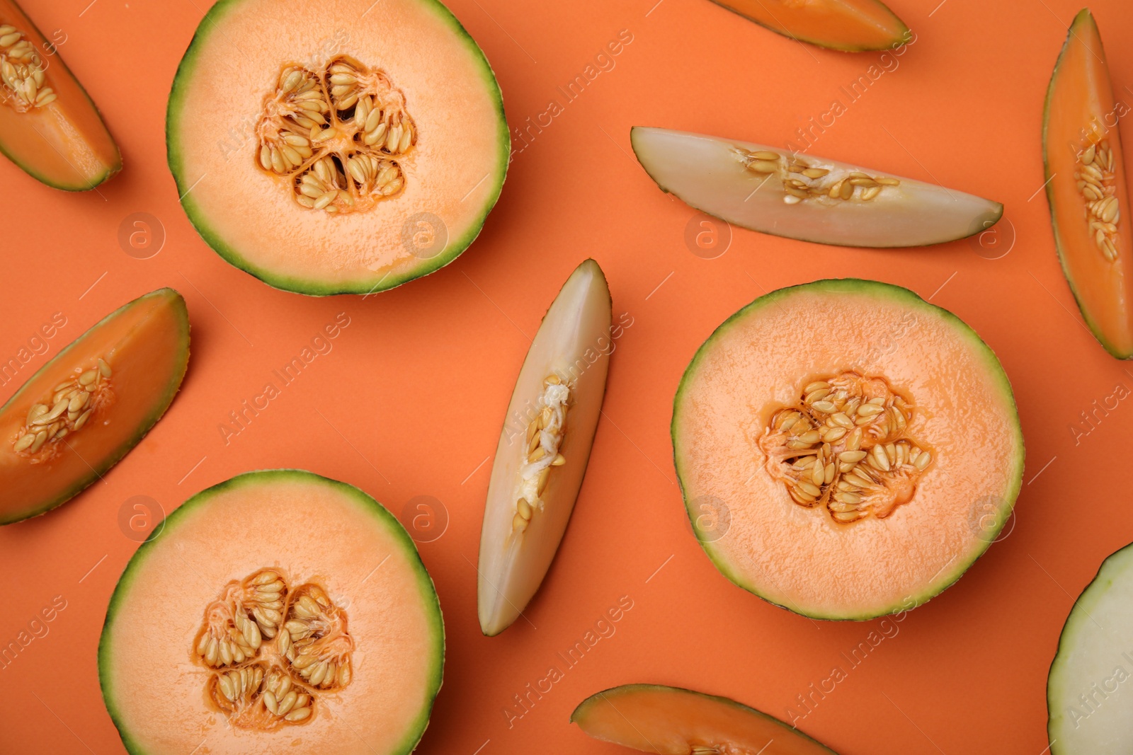 Photo of Cut different types of melons on orange background, flat lay