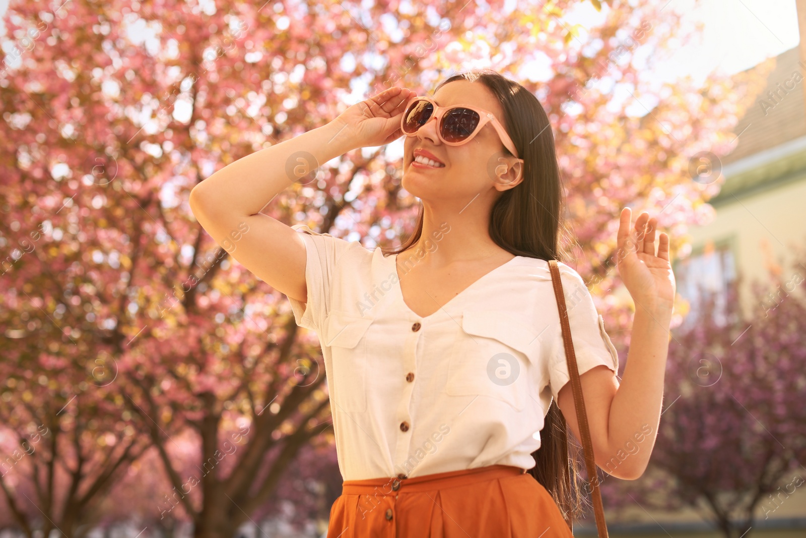 Photo of Happy stylish young woman near blossoming sakura tree outdoors. Spring look