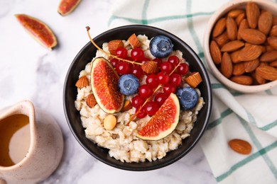 Photo of Bowl of oatmeal with berries, almonds and fig pieces on white marble table, flat lay