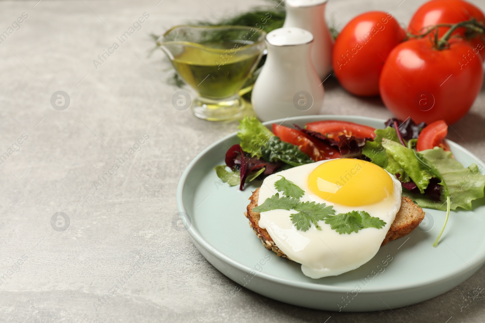 Photo of Plate with tasty fried egg, slice of bread and salad on light grey table. Space for text