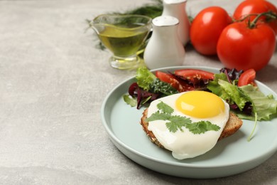 Photo of Plate with tasty fried egg, slice of bread and salad on light grey table. Space for text