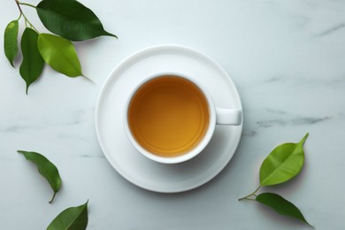 Photo of Green tea in cup with saucer and leaves on white marble table, flat lay