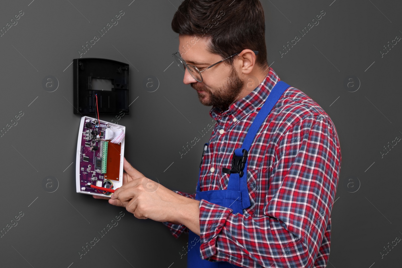 Photo of Technician installing home security alarm system on gray wall indoors