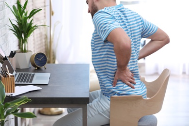 Photo of Young man suffering from back pain in office, closeup
