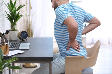 Young man suffering from back pain in office, closeup